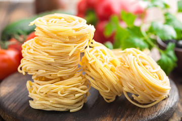 Raw all'uovo pasta, egg noodles with cooking ingredients on dark wooden rustic background, traditional italian cuisine