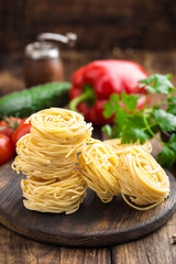 Raw all'uovo pasta, egg noodles with cooking ingredients on dark wooden rustic background, traditional italian cuisine