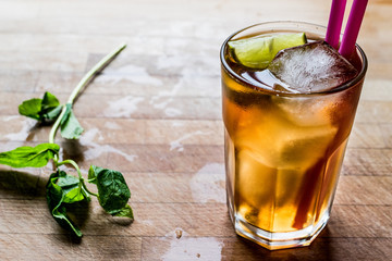 Long island iced tea cocktail with lime, ice and served with pink straw.