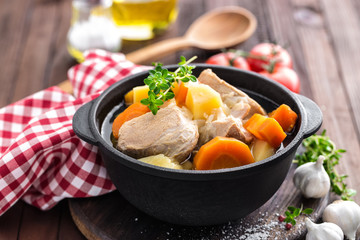 Meat stewed with carrots and potatoes in sauce on wooden rustic background