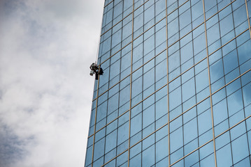 Cleaning service worker is cleaning glasses wall on a skyscraper with clouds in the sky background.