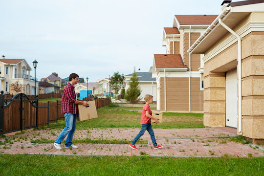 Young Man And His Son Carrying Boxes To Garage