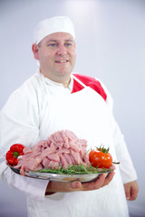A young chef has prepared a lot of meat for the dinner. He just cut it and put it on a big tray. Now, it is going to cook in the oven.