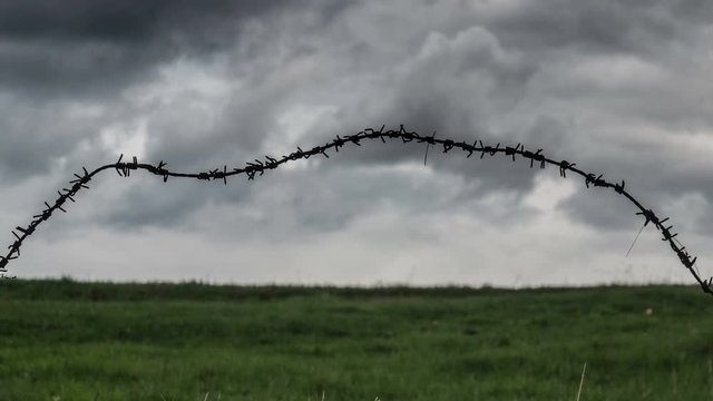 Barbed wire trembling in the wind on the dark stormy clouds background