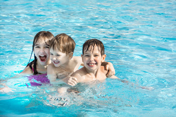 The older sister and younger brothers three are swimming and having fun in the pool with blue water