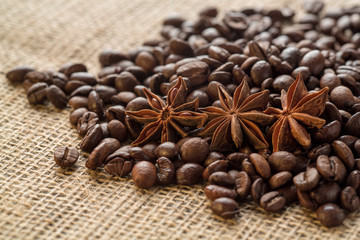 Coffee beans and illicium on a background of burlap. Roasted coffee beans background close up. Coffee beans pile from top with copy space for text. Seasoning. Spice. Badian. Coffee house.
