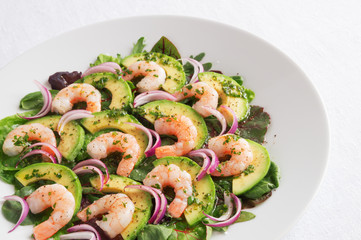 flat salad of prawns, avocado, and red onion on leafs mix sprinkled with black pepper and dressed with olive oil, lemon juice, and finely chopped parsley 