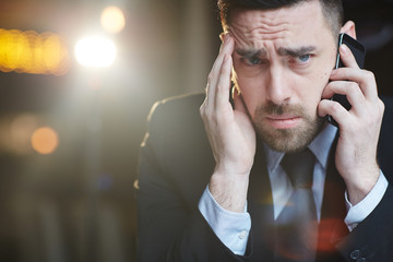 Portrait of modern bearded businessman talking by mobile phone with problem client looking confused...