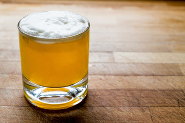 Whiskey sour cocktail with foam on wooden surface.