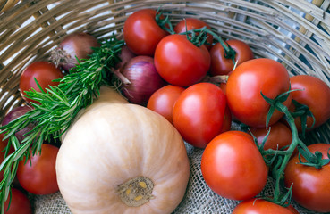Twig with tomatoes, onion, pumpkin and rosemary in a wicker basket.