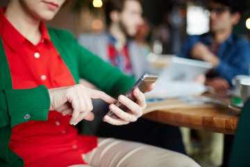 Closeup shot of young woman using smartphone in cafe, holding phone in hands and typing text message looking at screen with people in background