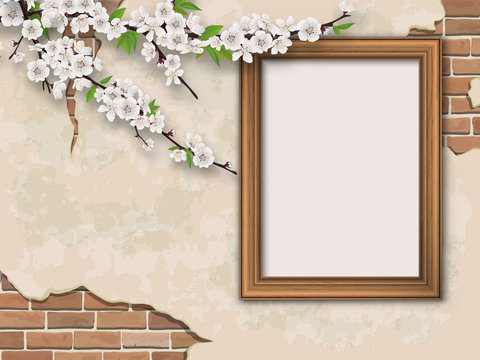 Blooming branches and golden picture frame on old wall background. Weathered plastered surface with cracks and brickwork.