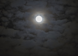 Soft shining full moon surrounded by moody fantasy-like clouds, night sky scene