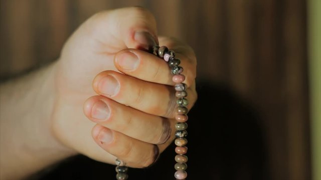 Man, lit hand close up, counts Malas, strands of beads used for keeping count during mantra meditations.