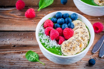 Healthy breakfast bowl: green spinach smoothie with banana, blueberries, raspberries, chia seeds and coconut