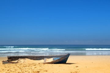 Fototapeta na wymiar Old fishing boat on the sunny beach of Atlantic ocean.