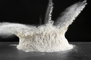 Pile of bursting flour on table against dark background