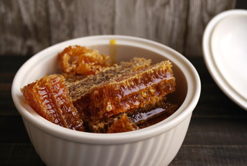 Honey comb in a deep white bowl on wooden table surface
