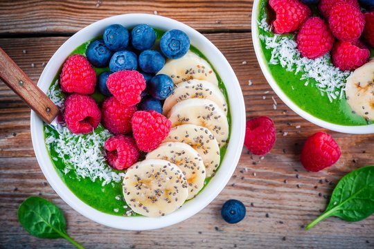 Healthy breakfast bowl: green spinach smoothie with banana, blueberries, raspberries, chia seeds and coconut