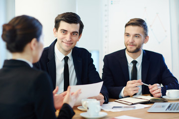Confident men looking at young co-worker and listening to her