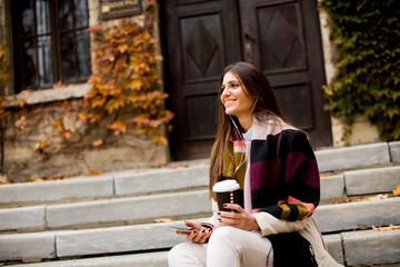 Young woman sitting outside, drinking coffee to go and holding a mobile phone in hand
