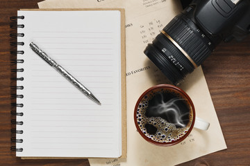 Coffee in cup, notebook and a DSLR camera on the table