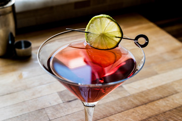 Cosmopolitan Cocktail with shaker on wooden surface.