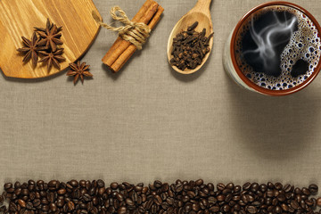 Cup of coffee, spices and roasted coffee beans on the rude textile background