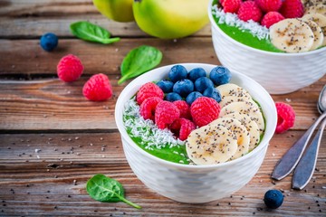 Healthy breakfast bowl: green spinach smoothie with banana, blueberries, raspberries, chia seeds and coconut