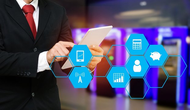 smart businessman in suit using his tablet, financial, business and technology concept with finance icon in hexagonal shaped pattern on blurred of ATM Machine for withdraw or deposit cash money.
