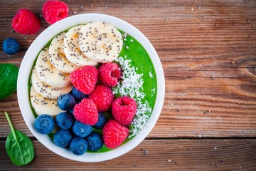 Healthy breakfast bowl: green spinach smoothie with banana, blueberries, raspberries, chia seeds and coconut