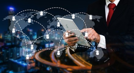 smart businessman in suit using his tablet, business and technology concept with world map social media network connection on blurred night city background, color tone effect.