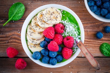 Healthy breakfast bowl: green spinach smoothie with banana, blueberries, raspberries, chia seeds and coconut
