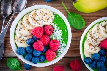 Healthy breakfast bowl: green spinach smoothie with banana, blueberries, raspberries, chia seeds and coconut