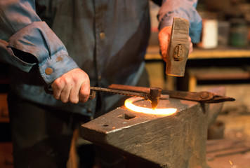 Fototapeta na wymiar Making of horseshoe. Male worker with hammer making nail holes on horseshoe.