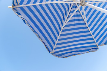Blick von unten auf einen blau-weiß gestreiften Sonnenschirm bei klarem Himmel