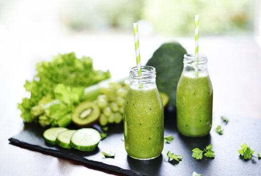 Green smoothie, healthy, organic drinks with fresh vegetables and fruits. Two smoothie glasses with drinking straw on a slate plate. Close-up shot.