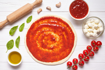 Pizza margherita cooking preparation. Raw pizza dough with baking ingredients: tomatoes sauce, mozzarella, basil, olive oil, cheese, spices. Italian food cuisine background. Flat lay.