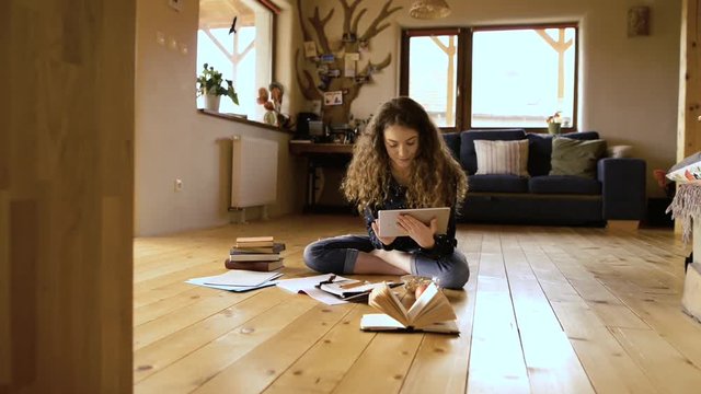 Teenage girl sitting on the floor holding tablet, studying