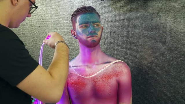 Makeup artist places the fairy lights to the young man with body art