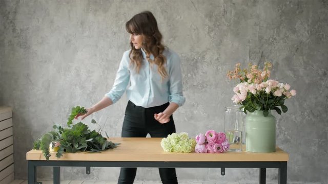 Florist at work: pretty young blond woman making fashion modern bouquet of different flowers, peone and roses
