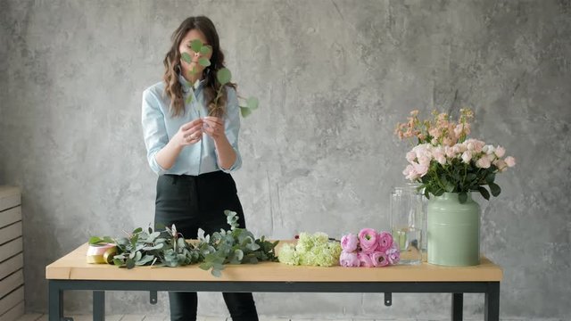 Florist at work: pretty young blond woman making fashion modern bouquet of different flowers, peone and roses