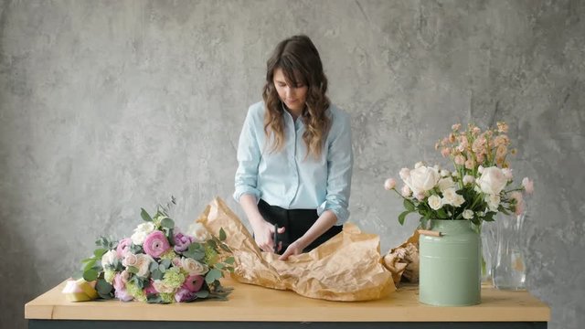 Florist at work: pretty young blond woman holds fashion modern bouquet of different flowers with peone and roses in craft paper