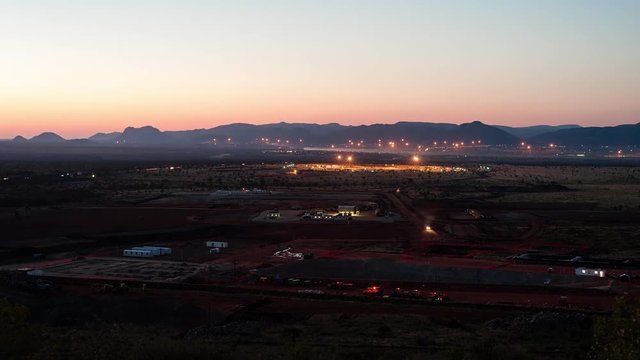 Static tilt up timelapse of a construction site on a mine while earthworks is in progress with heavy load machinery, trucks and tippers with stars in the night sky