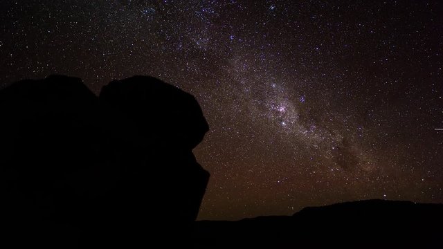 A scenic static day to night timelapse transition framed with rock boulders and a typical Karoo landscape in the distance, with the Milky Way twisting through a dark landscape scene