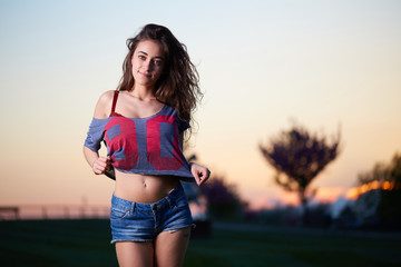 Beautiful brunette young woman with shortsand top posing above sunset background