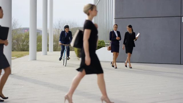  Businessman on bicycle arriving for work at office & greeting coworkers