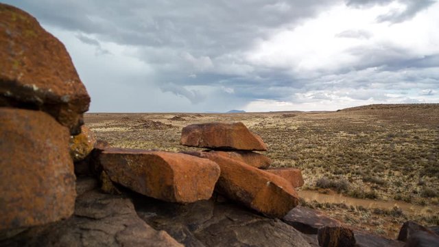 A linear timelapse of a rocky Karoo landscape with wide open vistas and stormy clouds gathering as a thunderstorm approaches while the camera moves in behind the rocks in the foreground