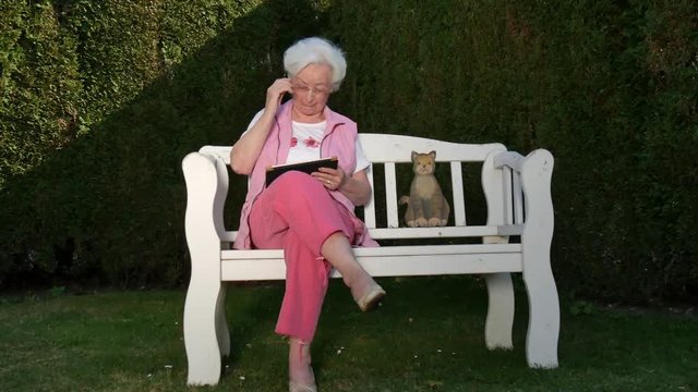Seniorin mit Tabletcomputer auf Gartenbank