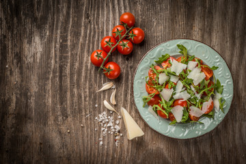 Rocket salad with cherry tomato and pecorino in plate on wooden tacbe, top view and copy space